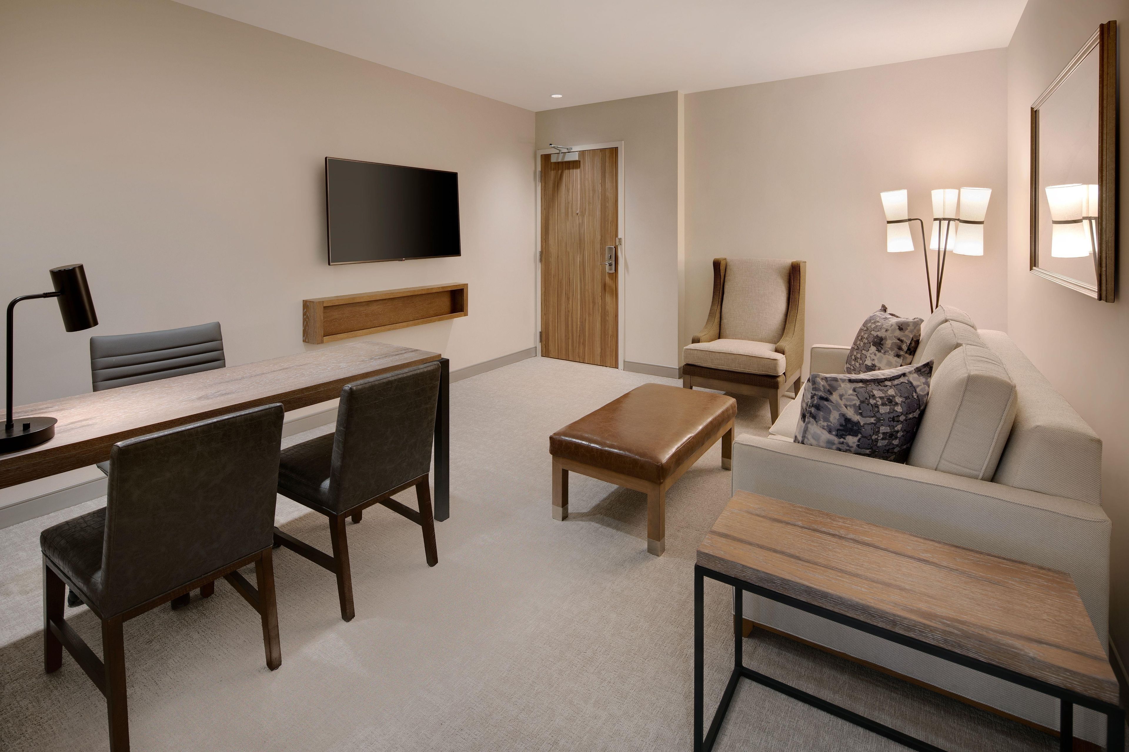 Une chambre d’hôtel moderne équipée d’un téléviseur à écran plat, d’un bureau avec des chaises, d’un canapé et d’une table basse.