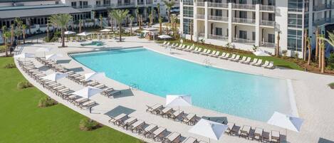 Un hôtel doté d’une grande piscine entourée de chaises longues et de parasols, ainsi que de plusieurs balcons et d’une pelouse bien entretenue.