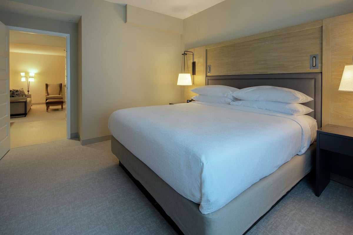 Une chambre d’hôtel avec un grand lit, une table de chevet, une lampe et une chaise dans un coin.
