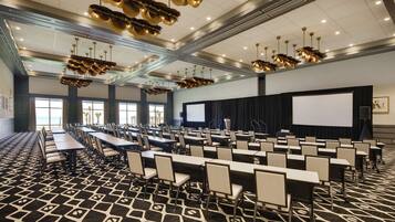 Un salón de conferencias con filas de mesas y sillas, una pantalla grande y un proyector.