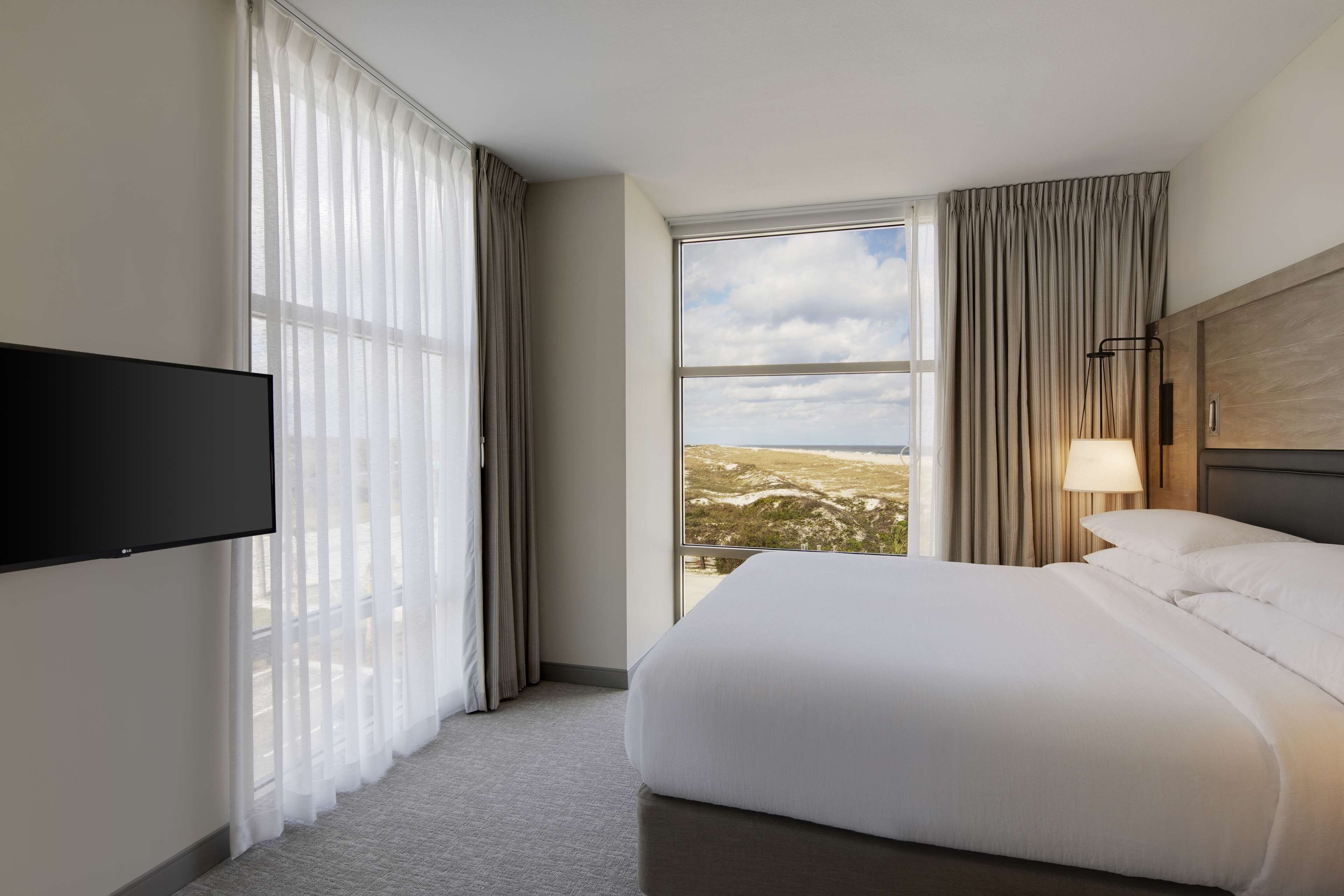 Een hotelkamer met een groot bed, een flatscreen televisie aan de muur, een raam met uitzicht op het landschap en een lamp op het nachtkastje.