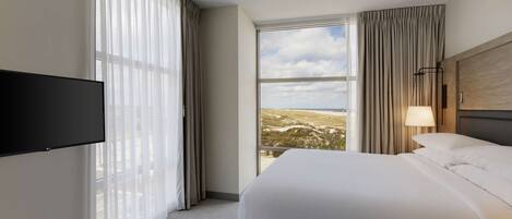 Een hotelkamer met een groot bed, een flatscreen televisie aan de muur, een raam met uitzicht op het landschap en een lamp op het nachtkastje.