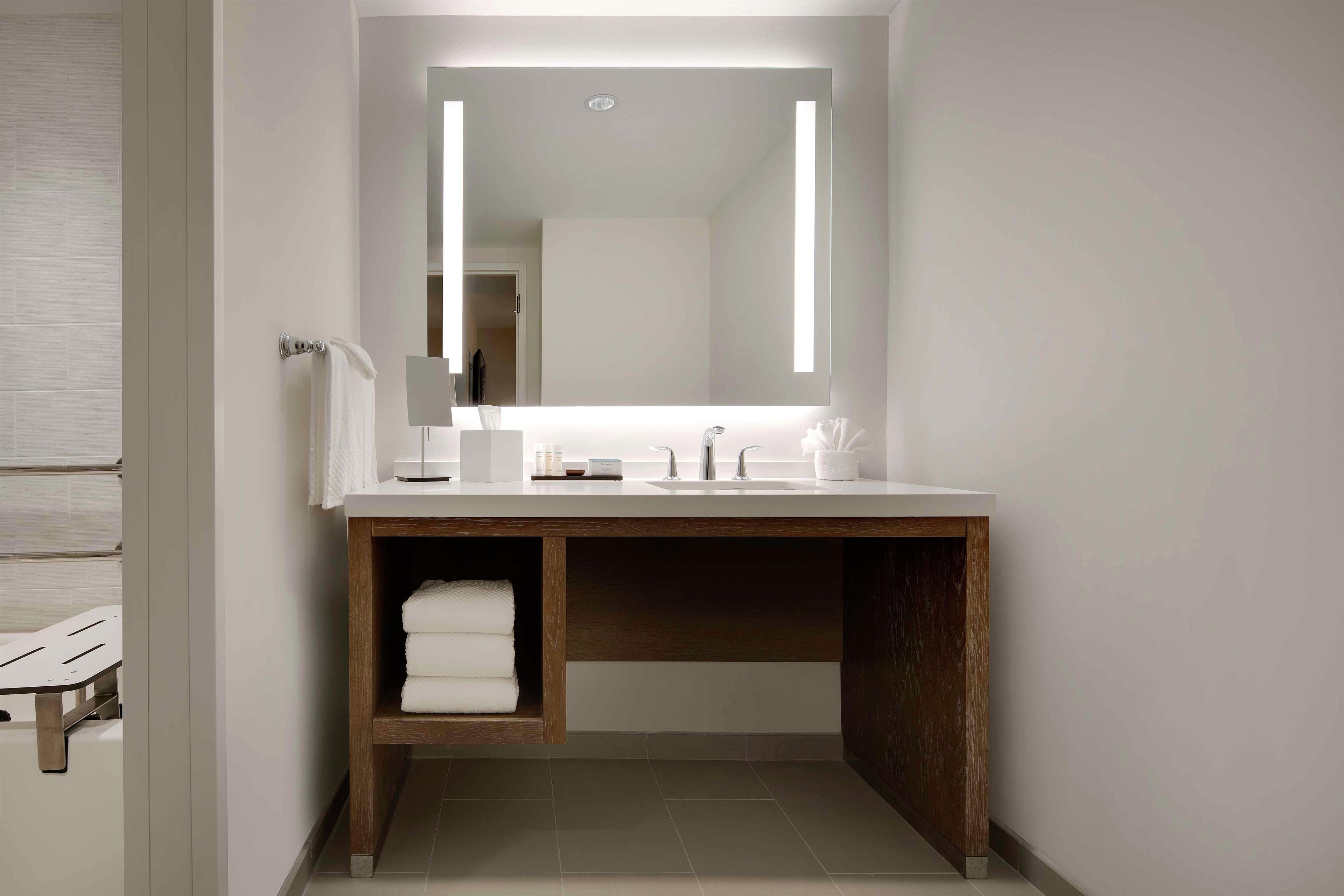 A modern bathroom with a large mirror, white countertop, and wooden vanity.