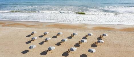 A beach with rows of sun umbrellas and lounge chairs aligned on the sand, facing the ocean.