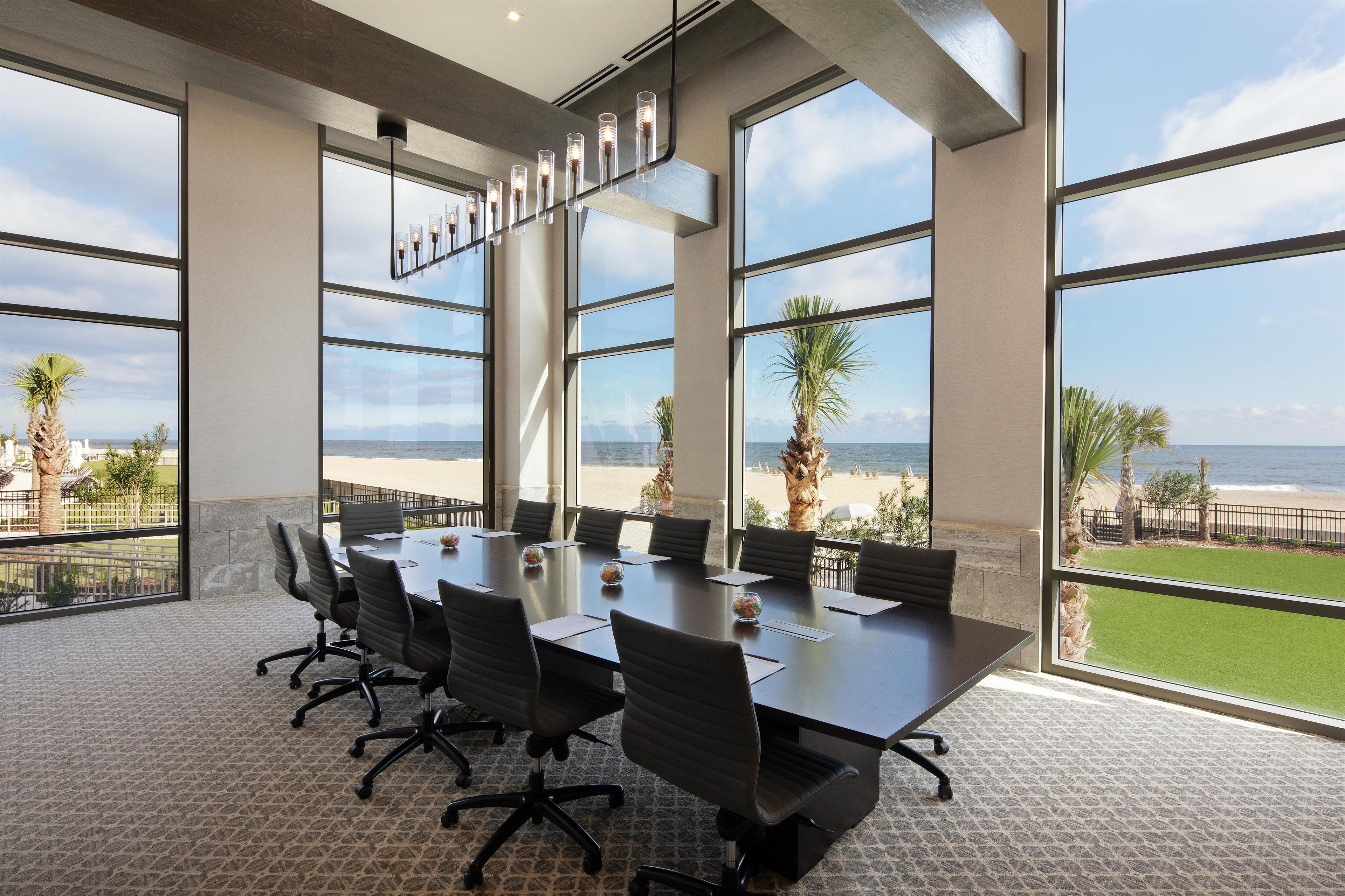 Ein Konferenzraum mit großem Tisch, Stühlen und Blick auf den Strand.