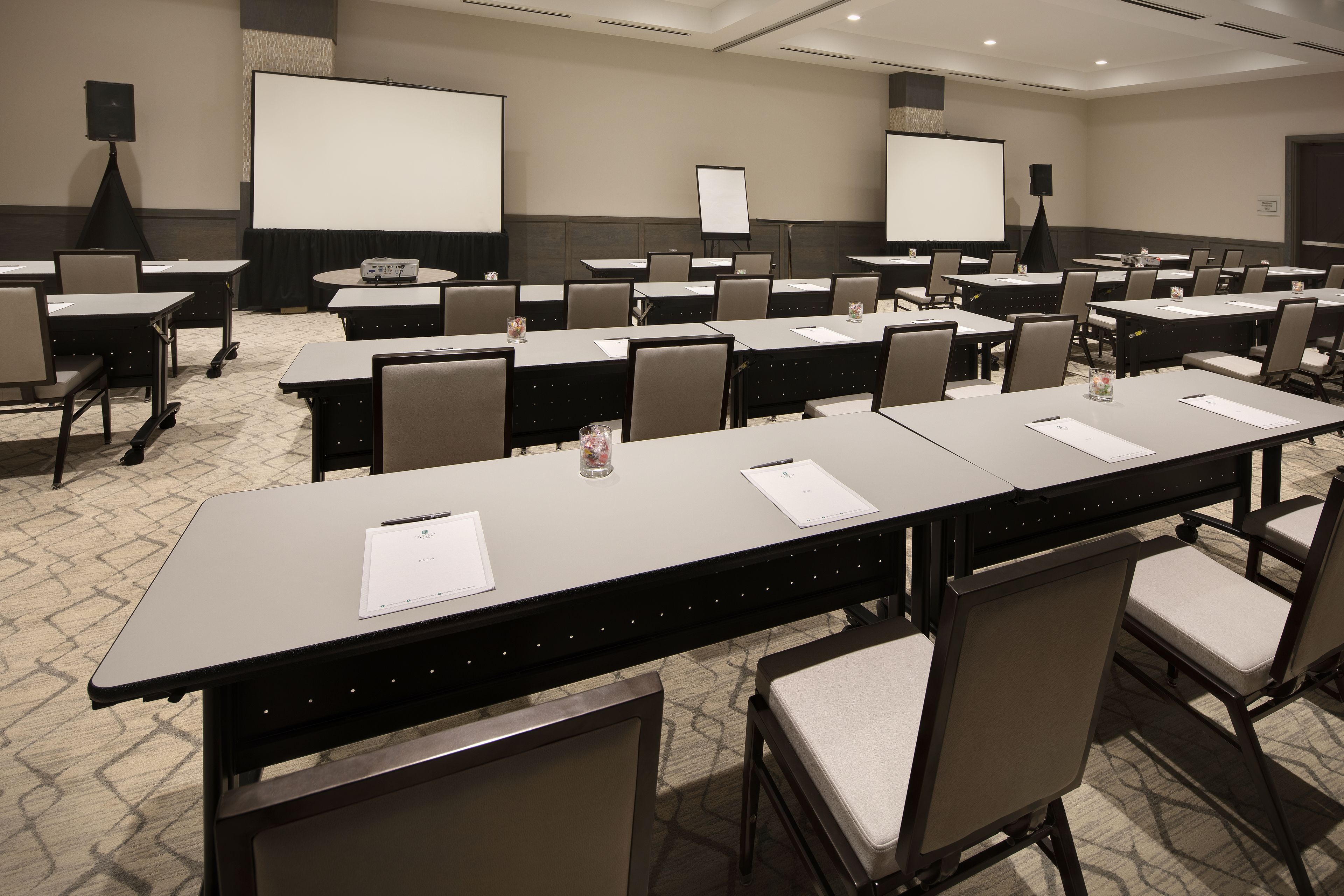 A conference room with long tables, chairs, a projector screen, and a whiteboard.