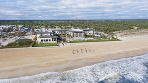 Un hotel frente a la playa con varias construcciones, una piscina y zona de playa.