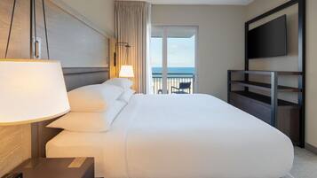 Habitación de hotel con una cama grande, televisión, escritorio con lámpara y vista al océano.