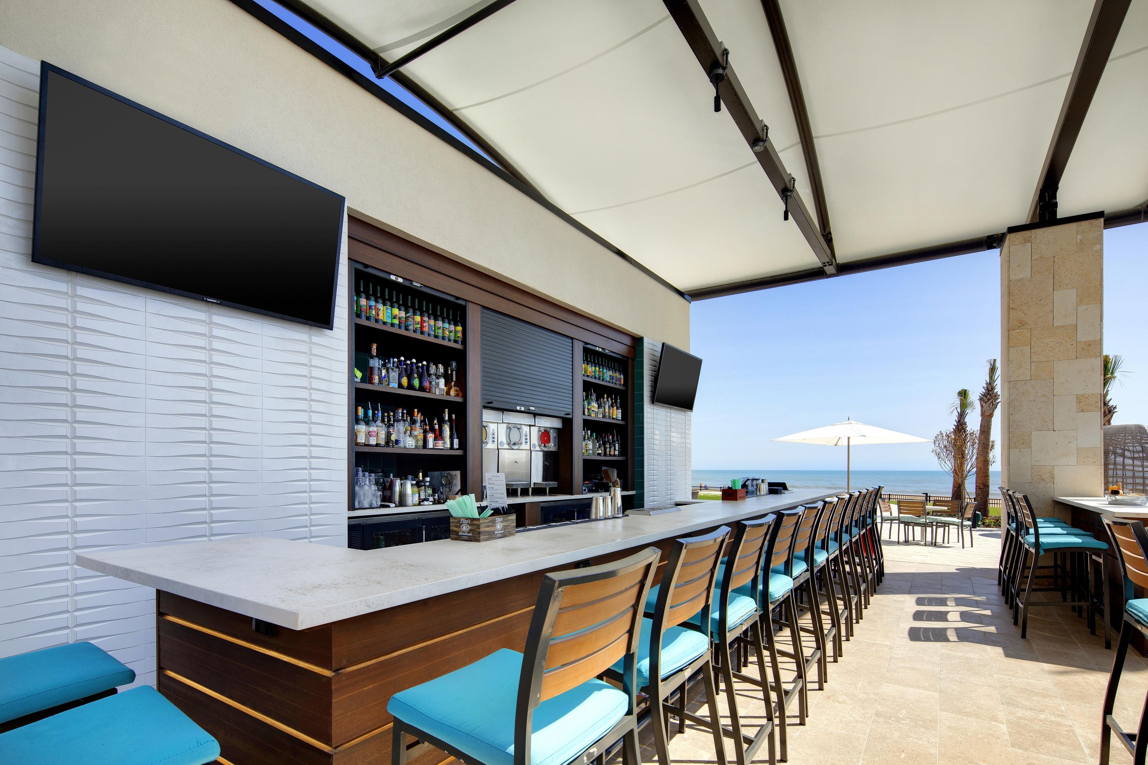 Un área de bar al aire libre con una barra larga, varias opciones de asientos y vista al mar.