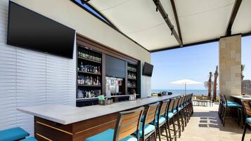 Un área de bar al aire libre con una barra larga, varias opciones de asientos y vista al mar.