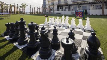 A large outdoor chess set on a checkered table in a courtyard with a building in the background.