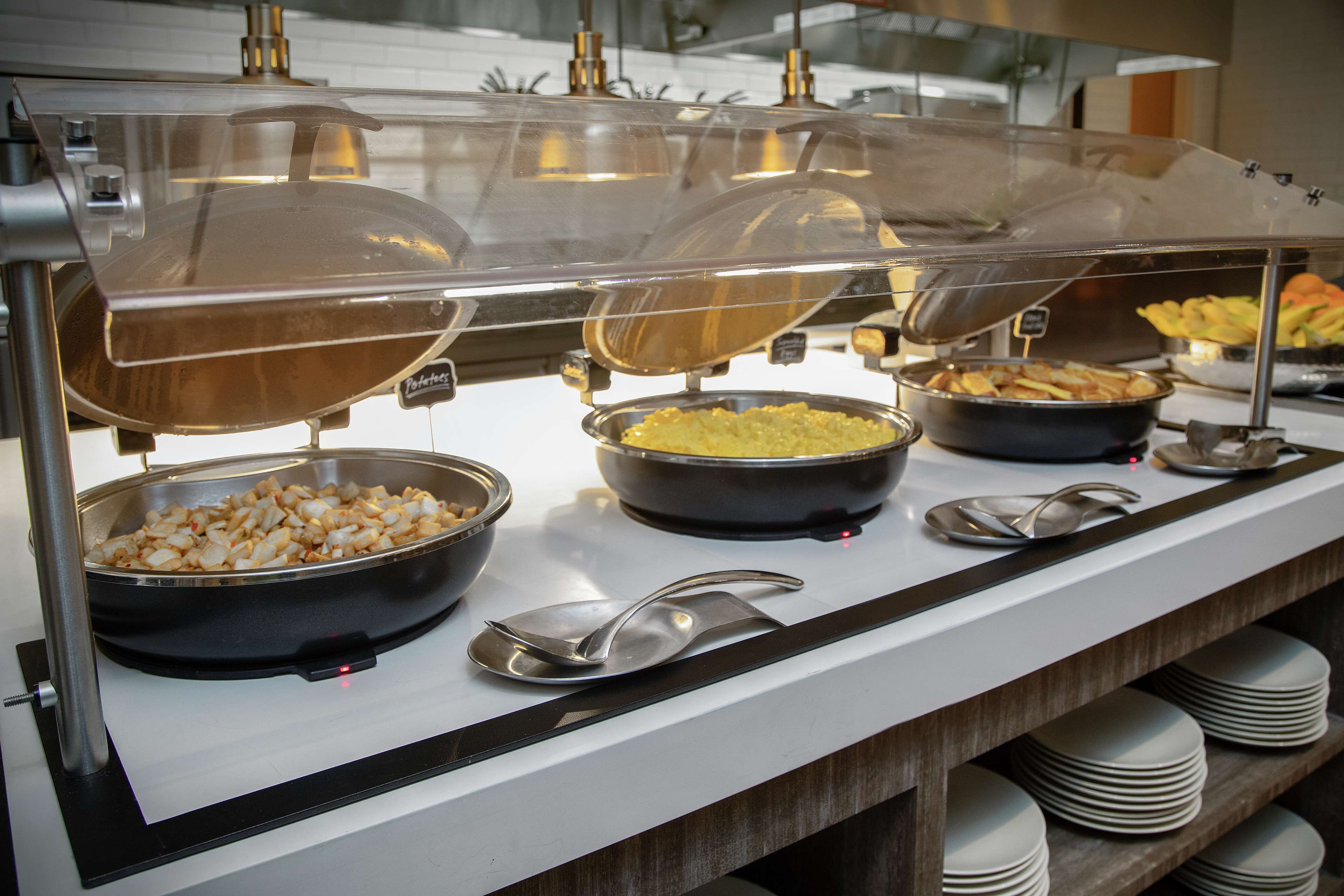 A buffet with various food items under protective covers.