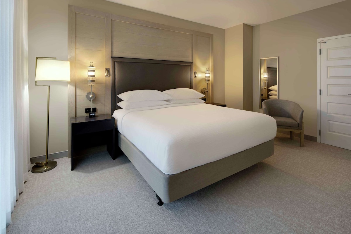 Une chambre d’hôtel bien aménagée, avec un grand lit, des lampes de chevet, une chaise et un miroir.