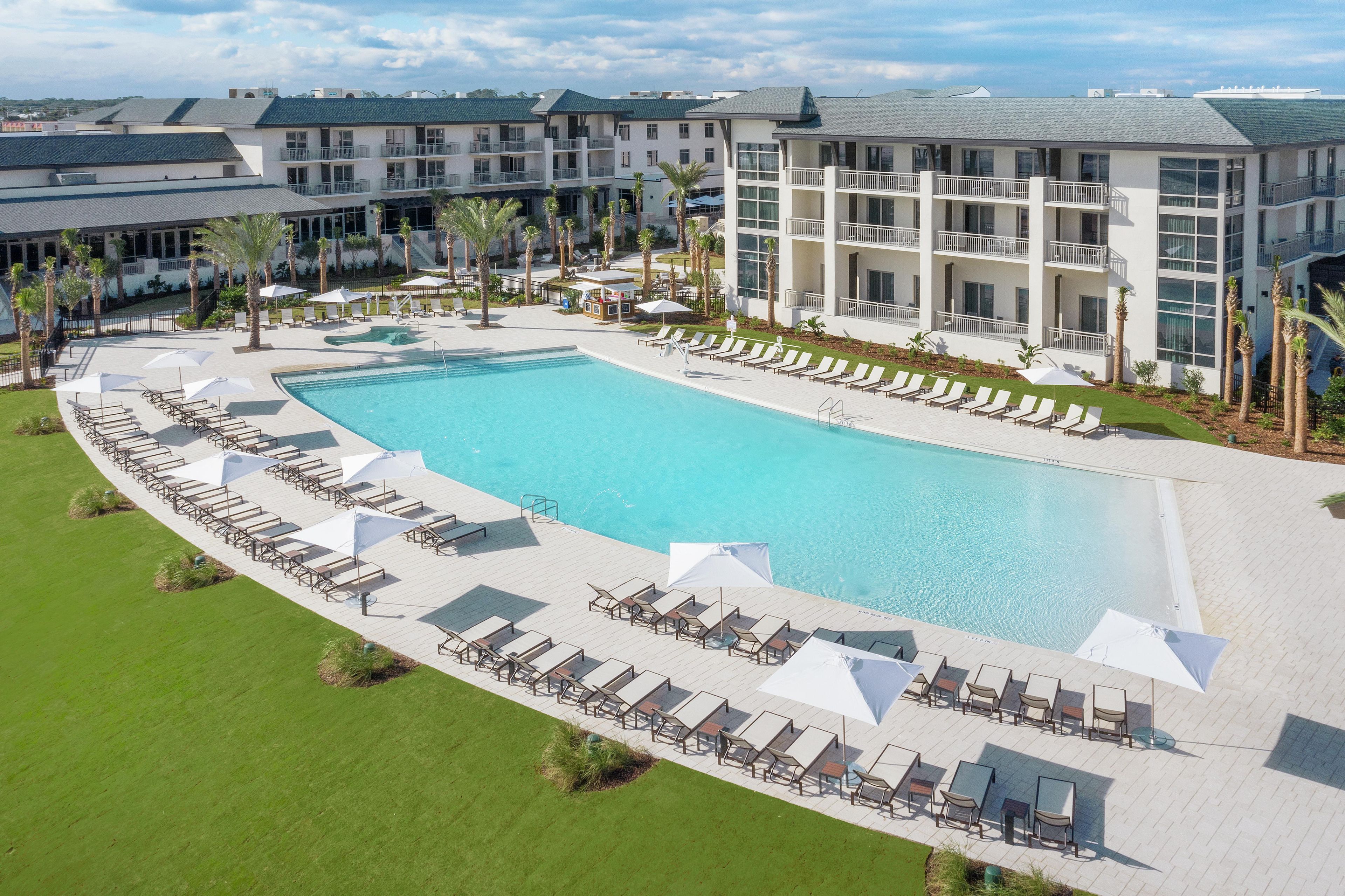 A large swimming pool with sun loungers and umbrellas, surrounded by a landscaped area with palm trees.