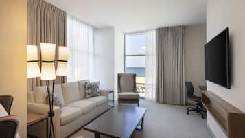 Habitación de hotel con sofá, sillón, mesa de centro y televisor montado en la pared.