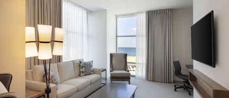 Een hotelkamer met een bank, fauteuil, salontafel en een aan de muur bevestigde televisie.