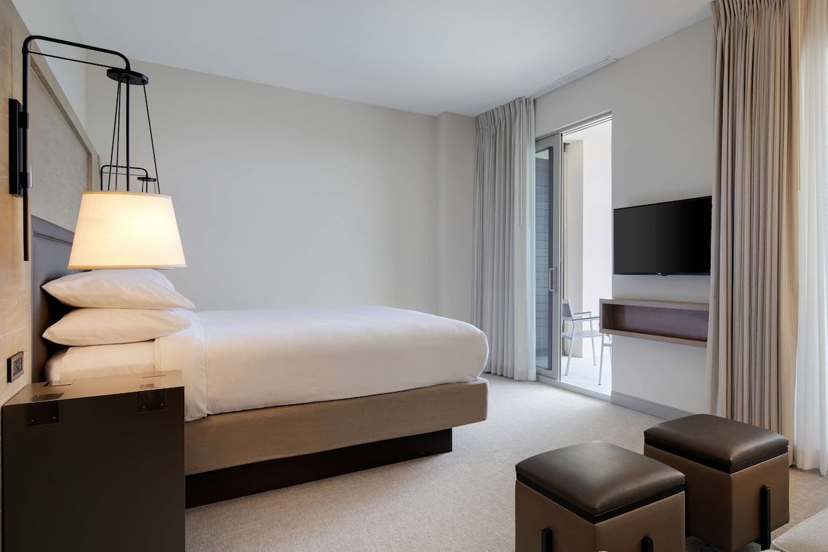 Une chambre d’hôtel avec un lit, un bureau doté d’une lampe, un téléviseur fixé au mur et une vue sur l’extérieur grâce à une porte coulissante.