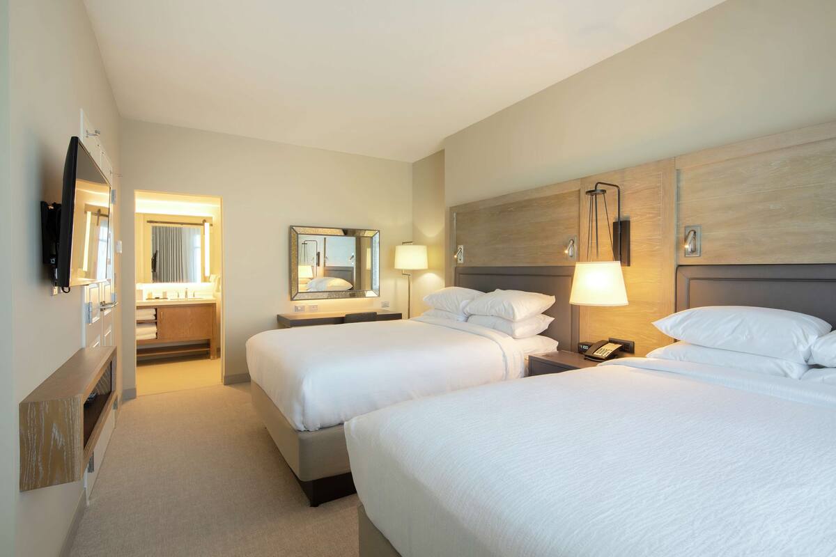 Une chambre d’hôtel avec deux lits, une salle de bain avec un miroir et une télévision.