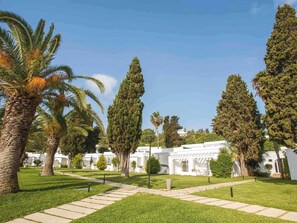 Un jardín ajardinado con palmeras y un edificio blanco de estilo arquitectónico moderno.