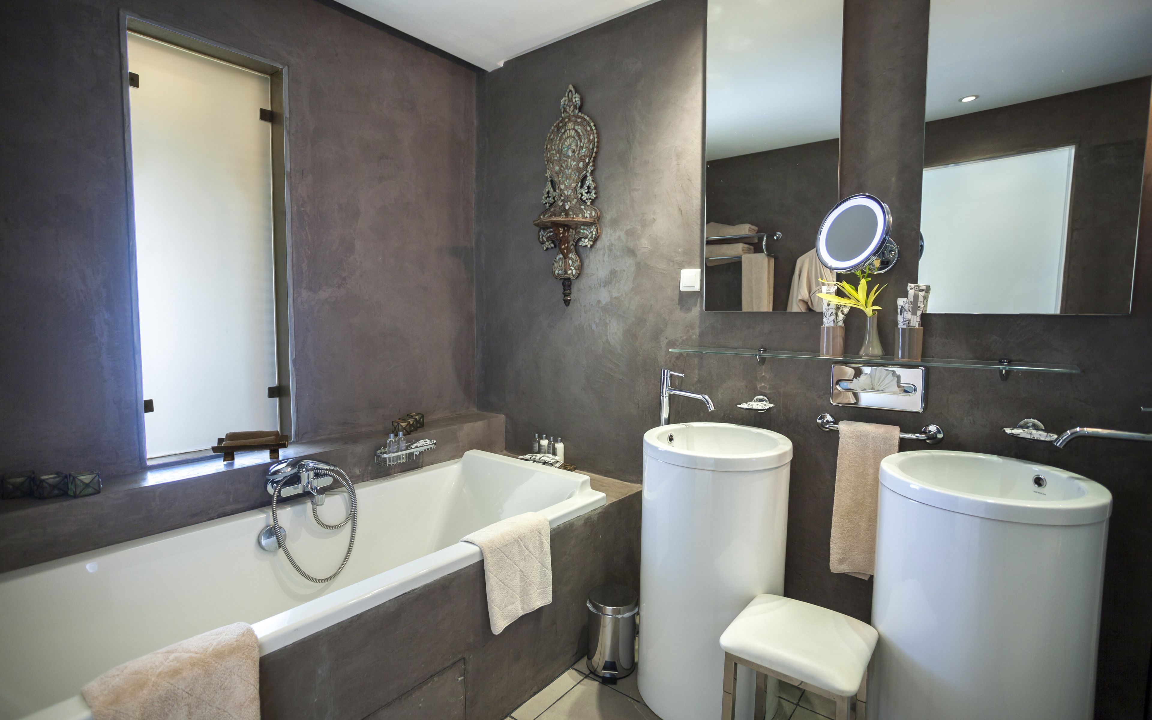 A modern bathroom with a bathtub, two sinks, a vanity mirror, and a decorative wall piece.