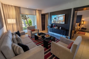 A modern living room with a sofa set, a coffee table, and a television mounted on the wall. - Mövenpick Hotel Gammarth Tunis (La Marsa)