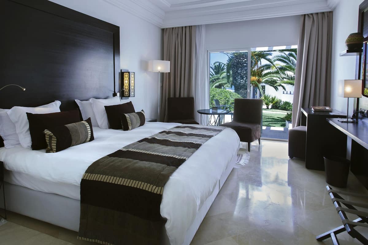 A hotel room with a large bed, a desk, a chair, and a view of the outdoors.