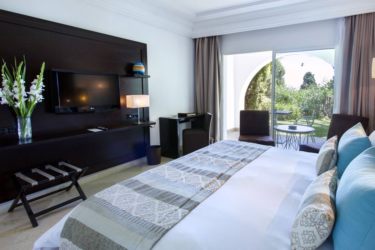 Une chambre d’hôtel avec un grand lit, un bureau, une télévision et un balcon équipé d’une table et de chaises.