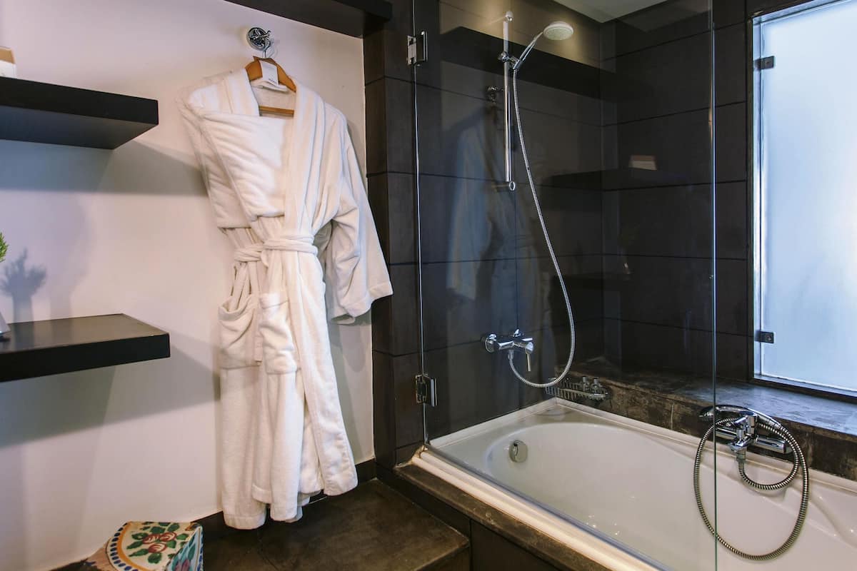 Un baño moderno con ducha envuelta en cristal, una bañera y una bata blanca colgada en un perchero.