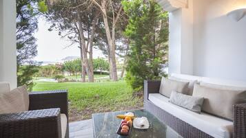 Un área de estar moderna al aire libre con muebles de mimbre, una mesa de vidrio con frutas y una servilleta, y vistas a un jardín exuberante y un paisaje lejano.