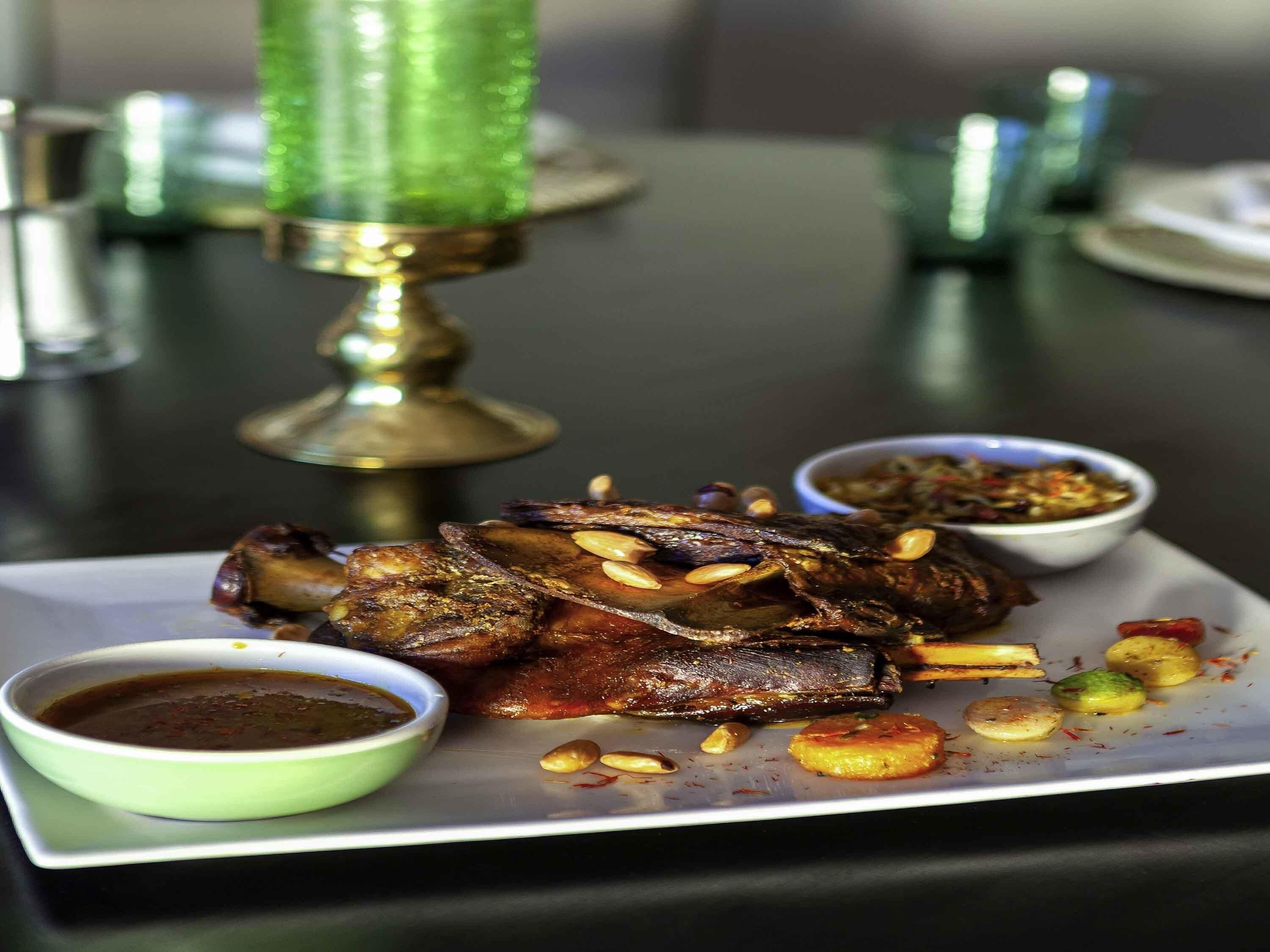 Une assiette avec de la viande rôtie, deux petits ramequins de sauce et une bougie décorative.