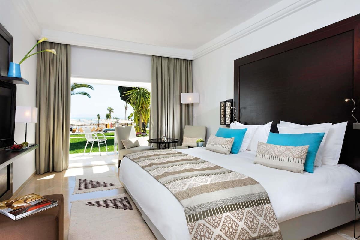 Une chambre d’hôtel avec un grand lit, une télévision, un bureau et une vue sur la plage.