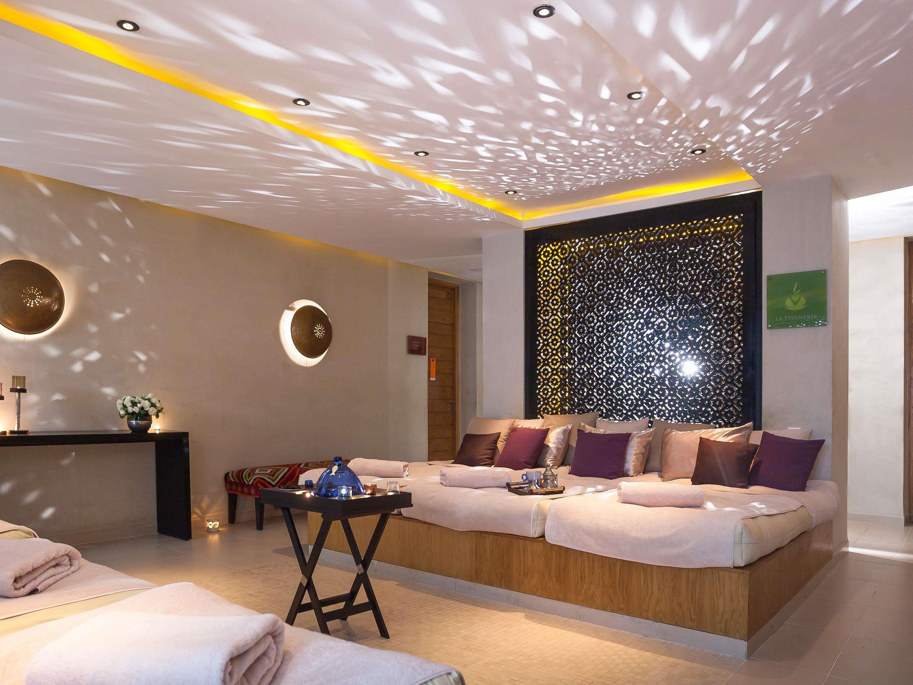 A modern spa room with a wooden reception desk, a sofa with cushions, and a decorative wall panel.
