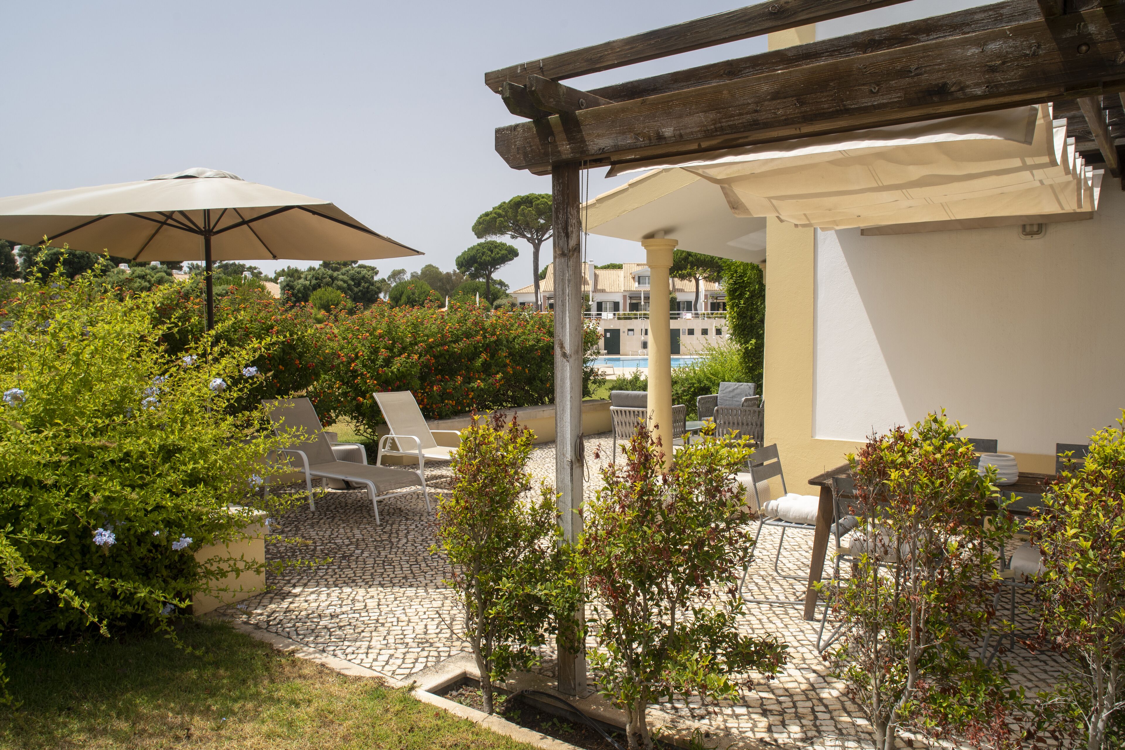 An outdoor patio area with lounge chairs, umbrellas, and a pool in the background.