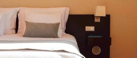 A neatly made bed with a white and orange bedspread, a black nightstand with a lamp, and a wooden floor.
