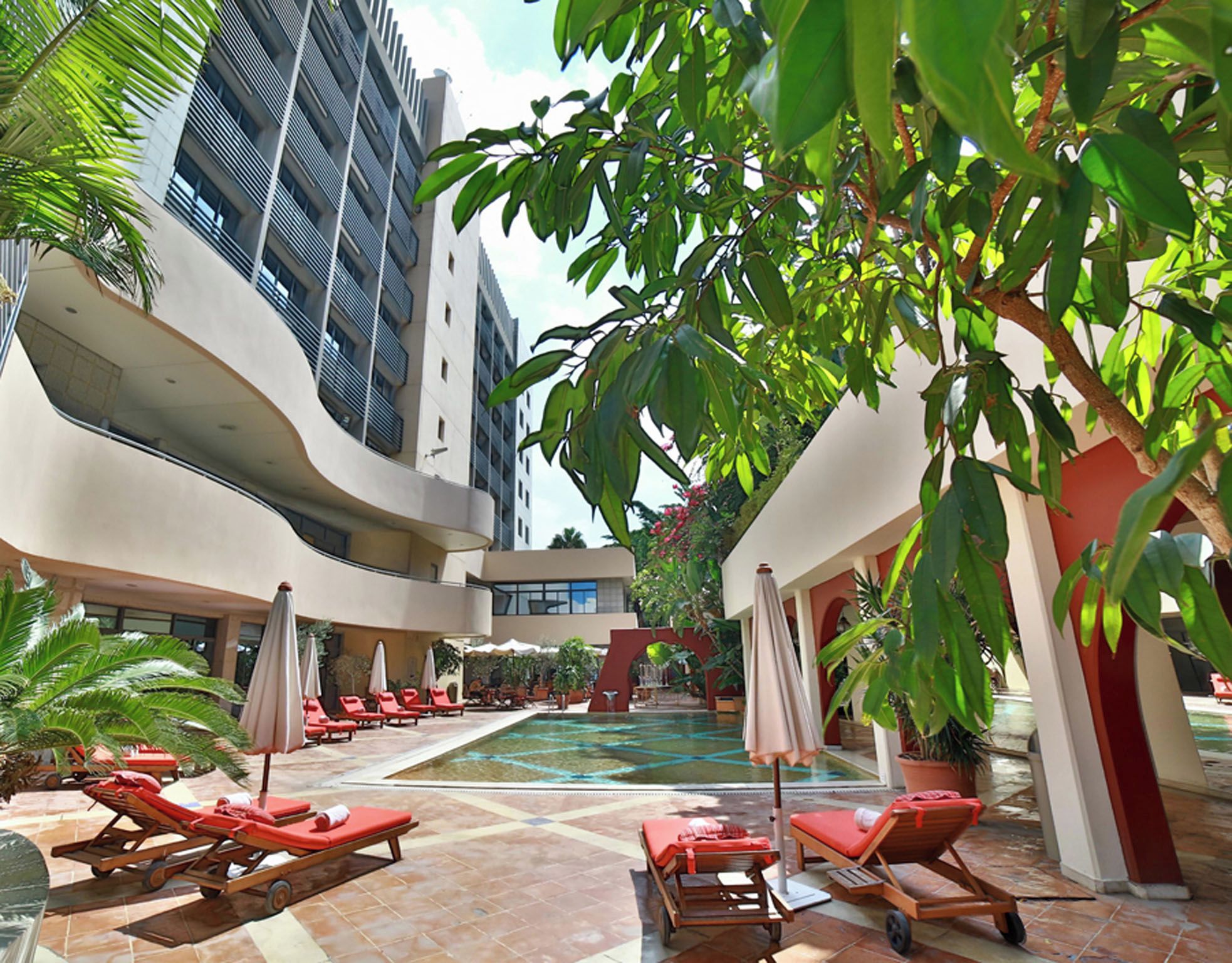 A hotel courtyard with a pool, lounge chairs, and a modern building with balconies.