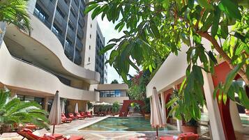A hotel courtyard with a pool, lounge chairs, and a modern building with balconies.
