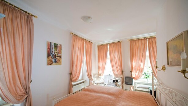 A bedroom with a large bed, two windows with curtains, a small table with a chair, a television, and a painting on the wall. - Goldener Hecht (Heidelberg)