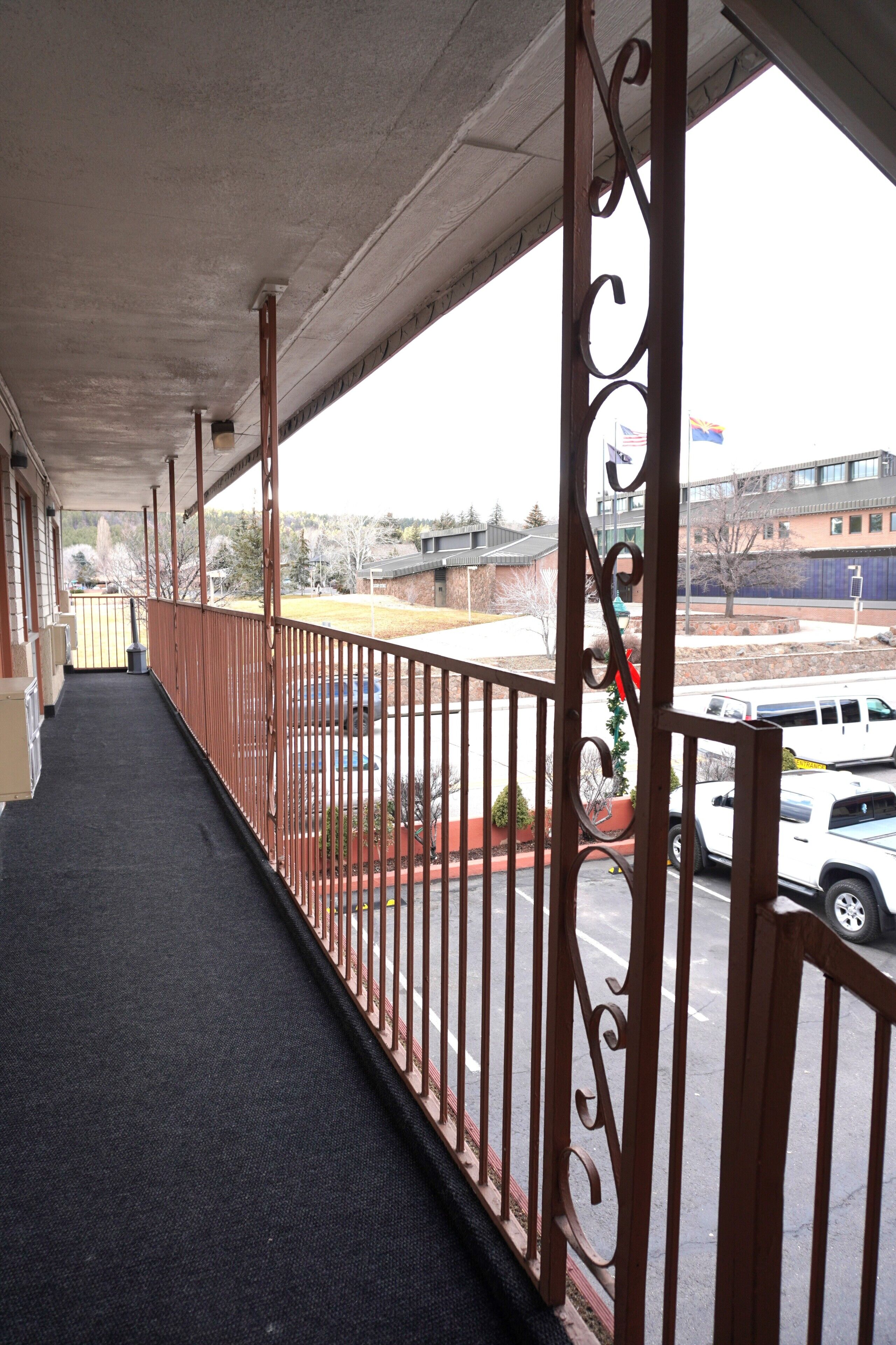 A covered outdoor area with a metal railing, a concrete ceiling, and a view of a parking lot and buildings in the background.