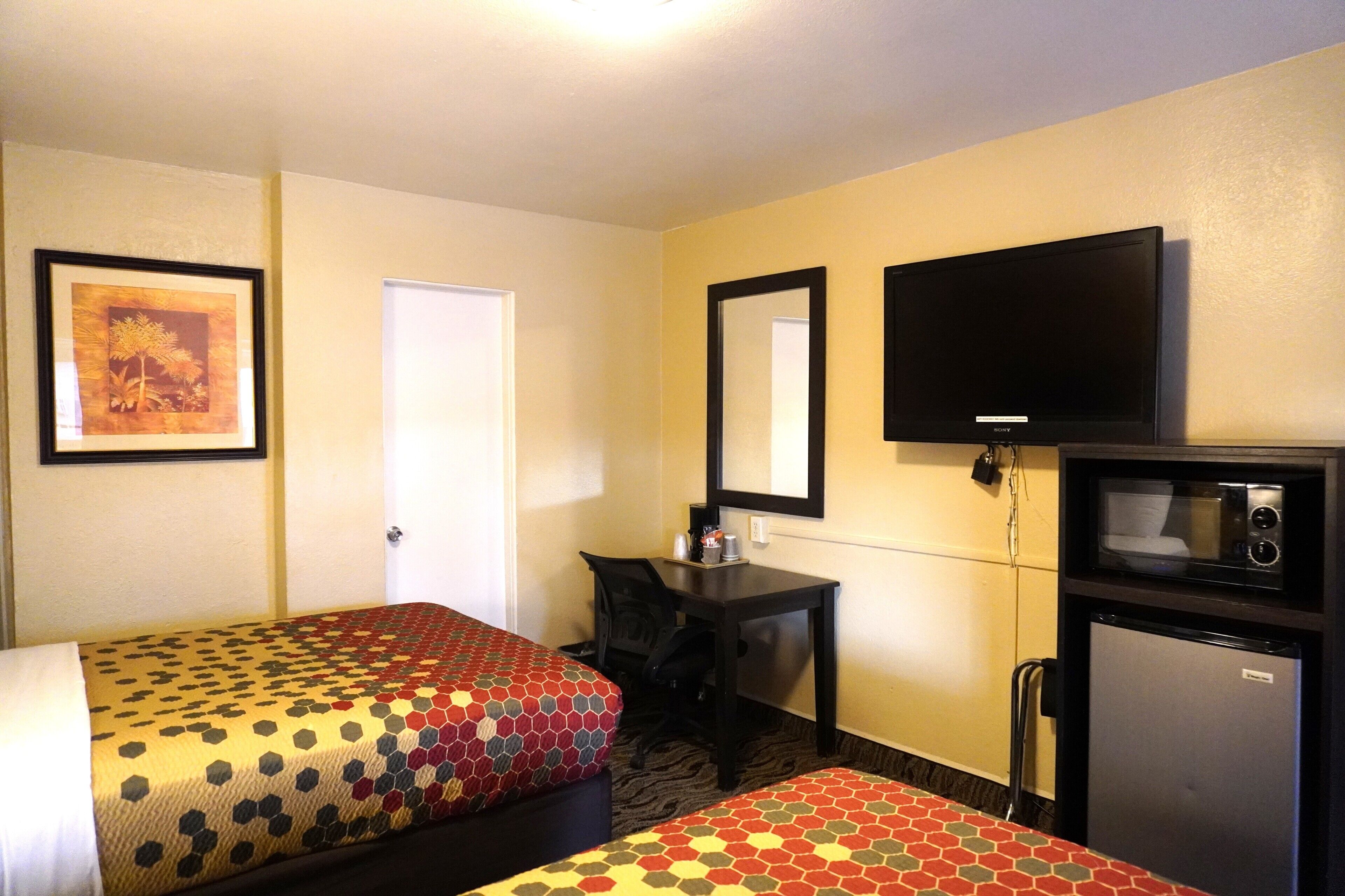 A hotel room with two beds, a desk, a television, and a refrigerator.
