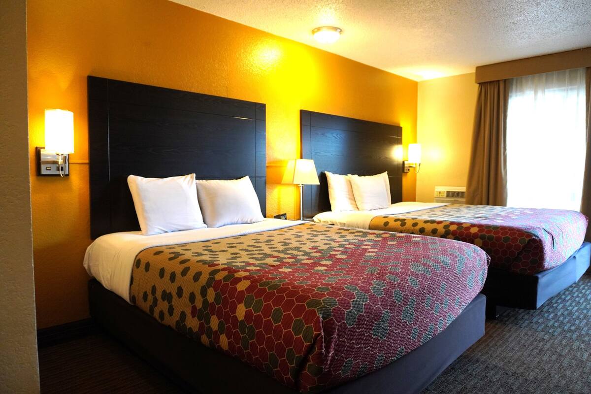 Habitación de hotel con dos camas, cada una con cabecera, lámparas de noche y colcha estampada.