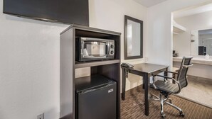 Ein kompaktes Hotelzimmer mit Küchenzeile, Schreibtisch, Stuhl und einem großen Spiegel.