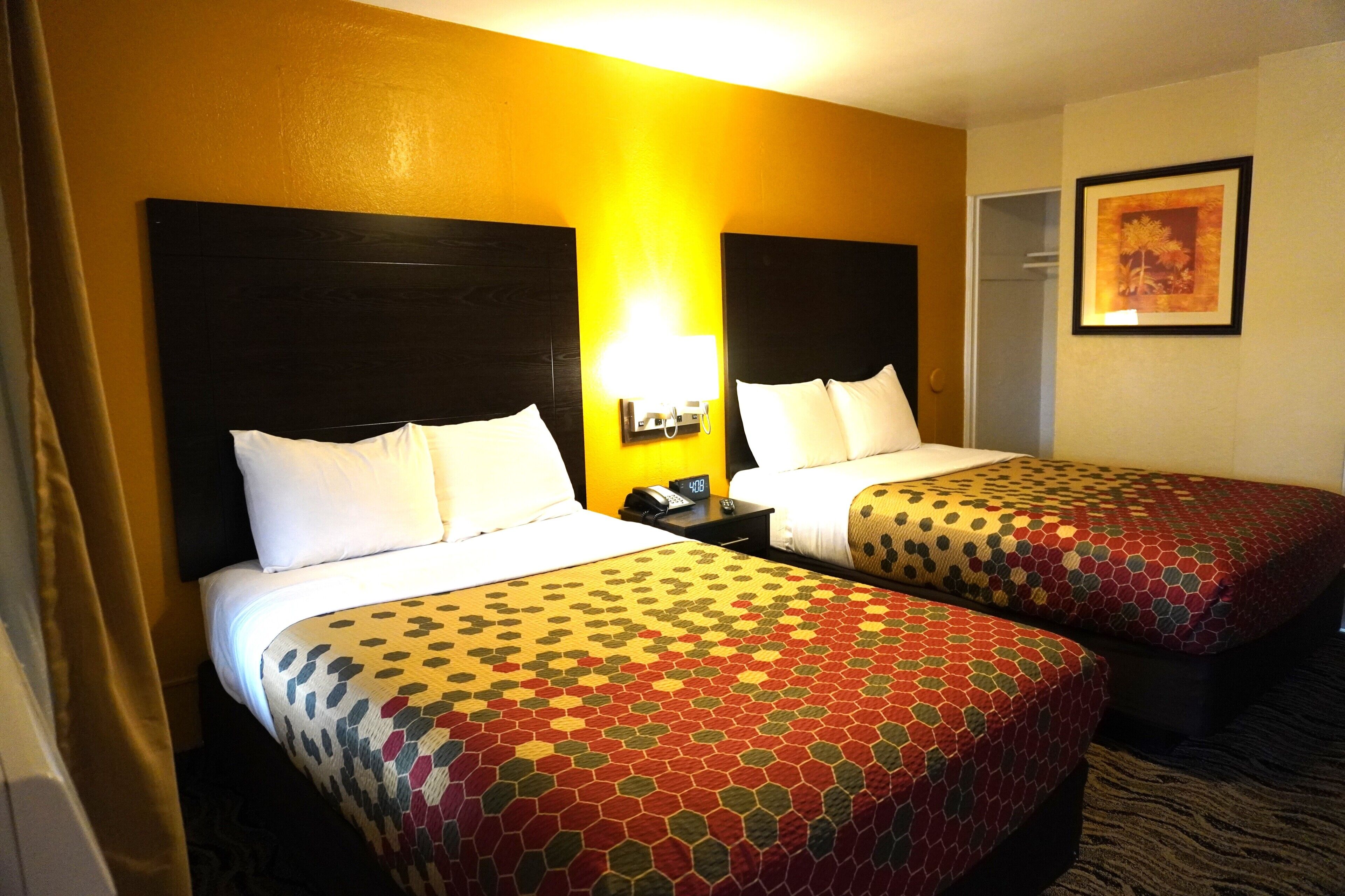 A hotel room with two beds, a nightstand with a phone and lamp, and a framed picture on the wall.