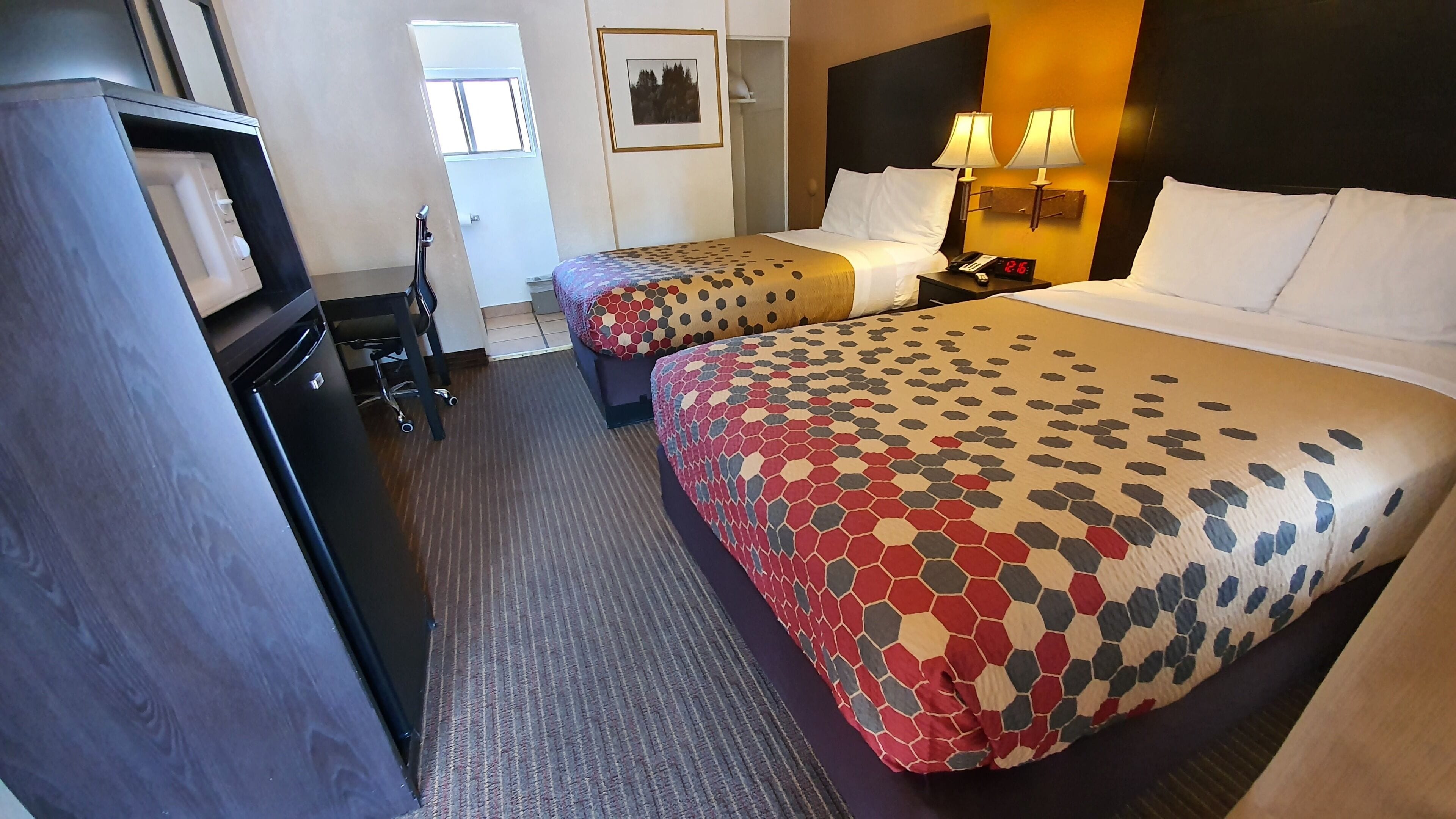 A hotel room with two beds, a desk, a chair, a wardrobe, and a bathroom.
