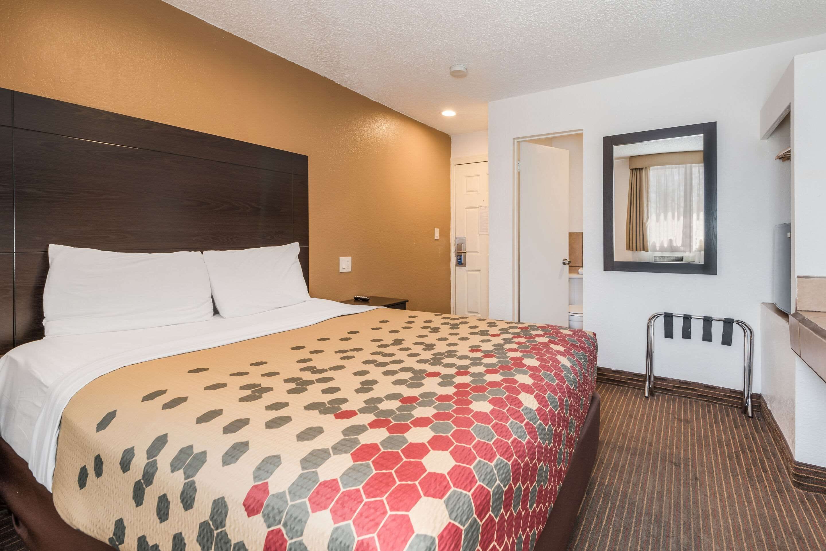 A hotel room with a large bed, a wooden headboard, a mirror, a small table, and a coat rack.