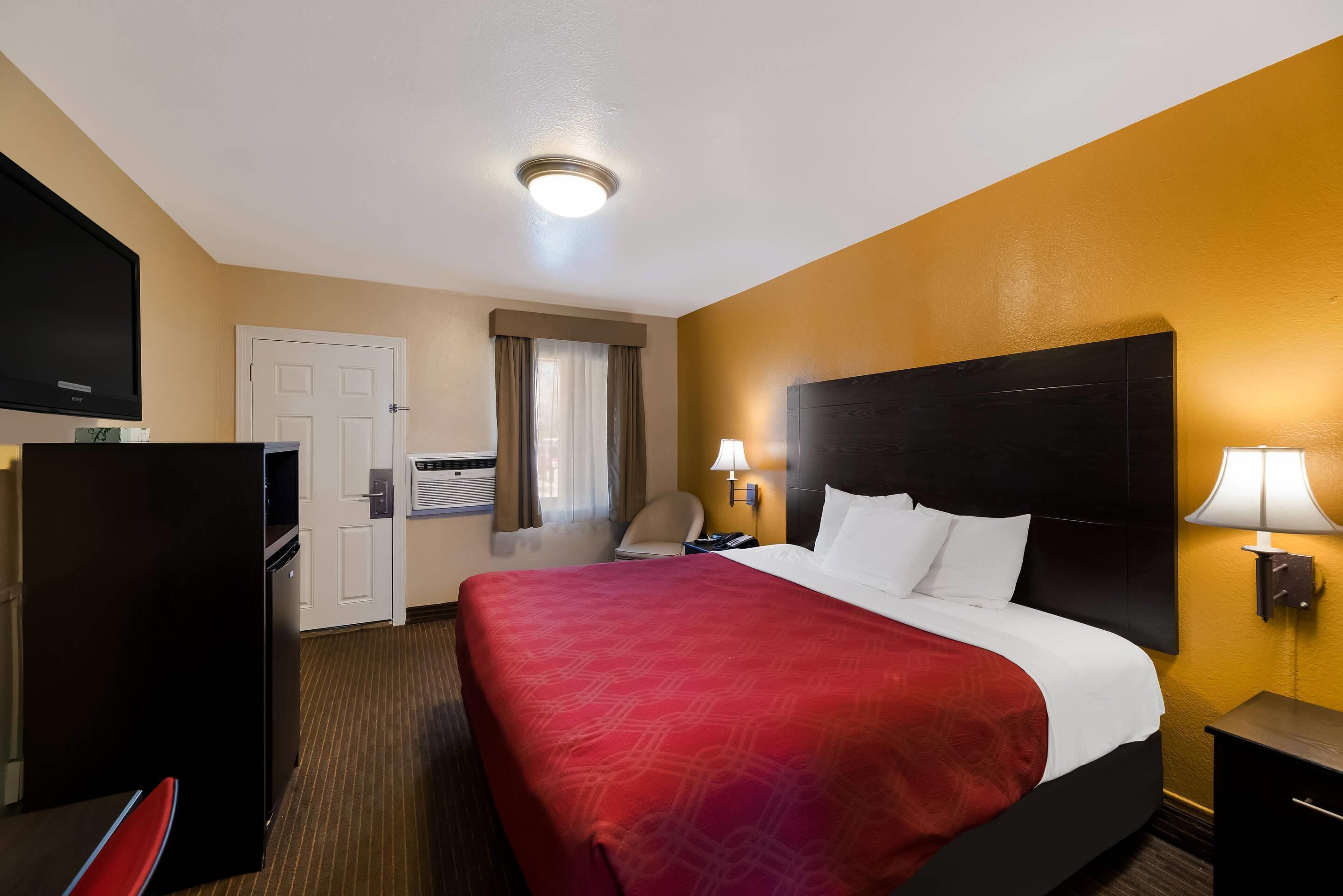 A hotel room with a bed, a desk, a television, and a door.