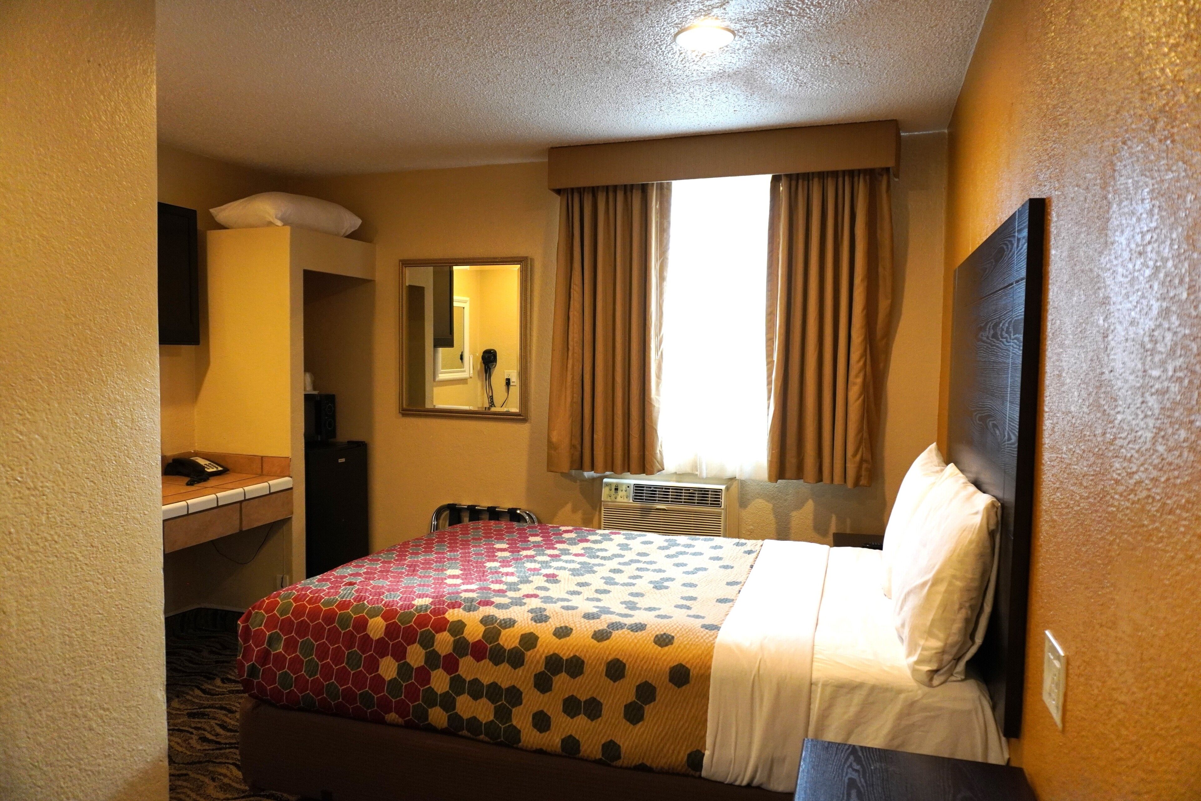 A hotel room with a bed, a desk, a chair, a mirror, and a window with curtains.