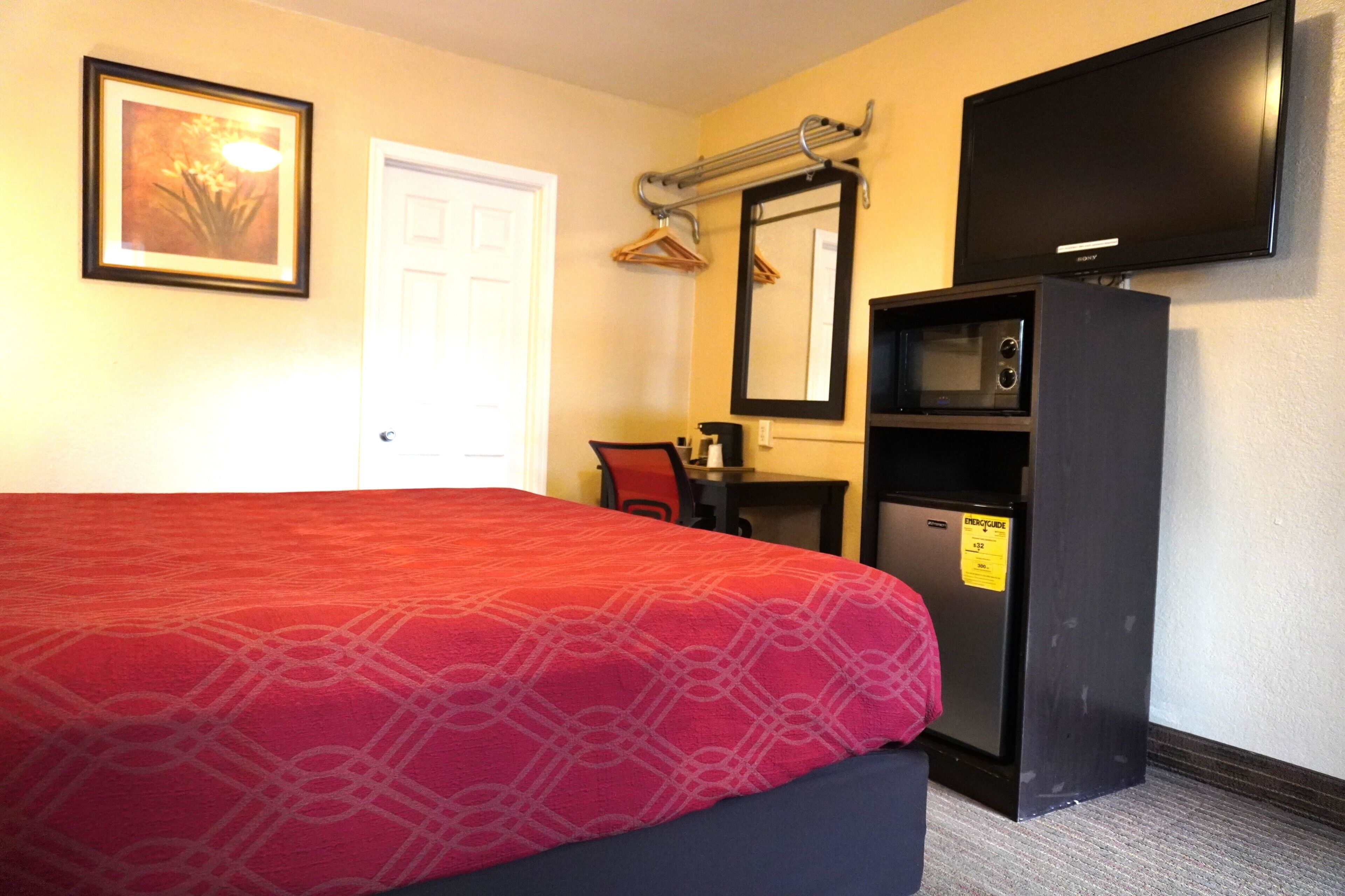 A hotel room with a bed, a desk with a computer, a TV, and a microwave.