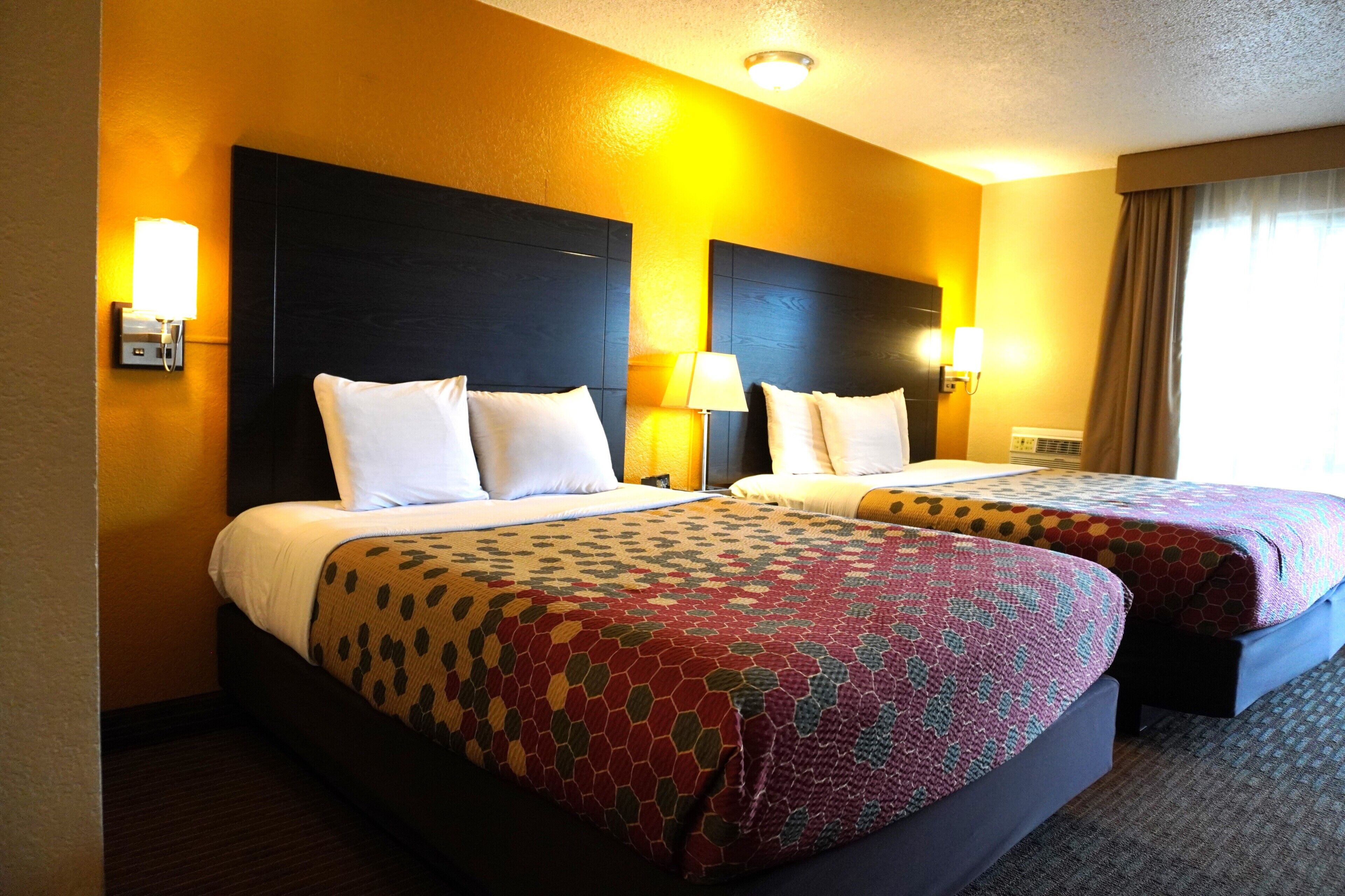 A hotel room with two beds, each with a headboard, bedside lamps, and a wall-mounted telephone.