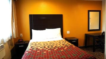 A hotel room with a bed, a nightstand with a clock, a desk, and a chair.