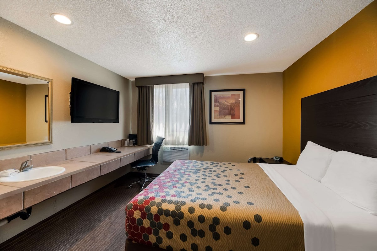 Habitación de hotel con cama, escritorio con silla, lavamanos y televisor.